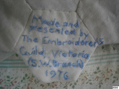 Embroidered inscription in blue thread on a plain hexagonal piece of fabric