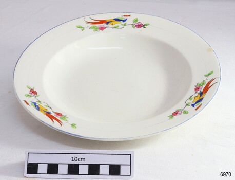 White plate with blue rim and decorated with motifs of a bird of paradise above floral branch