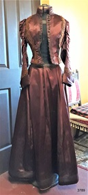 Evening outfit of a long-sleeved jacket with flared waist and high collar, and a long, gently gathered skirt.