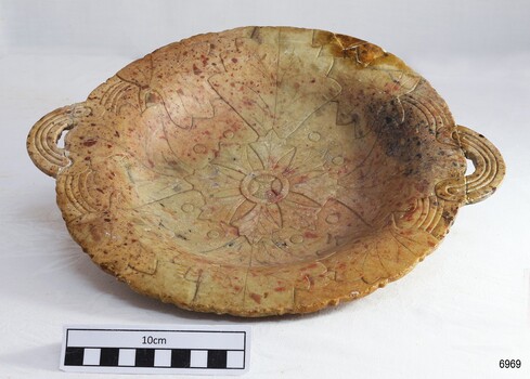 Light brown alabaster bowl is etched with a design. It has two round handles of the same material.