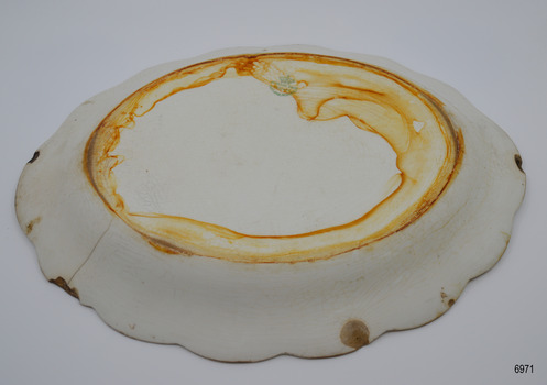 Oval plate has green maker's stamp. Surface has brown water stain, crazing, chips and a crack.