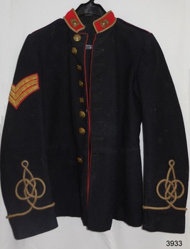 Dark coloured tunic, long sleeves, single breasted. Red band collar with brass badges. Brass buttons. Sergeant stripes. 