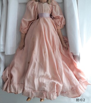 A pink satin doll's dress with gathered sleeves, a frill along the hem, a pink ribbon tied at the waist and a beaded neckline.