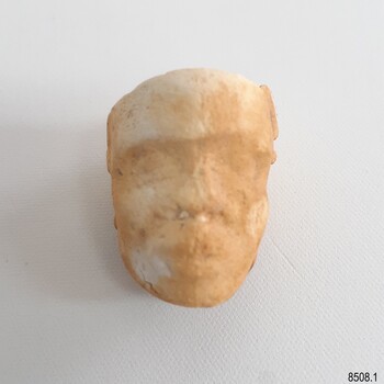 White clay tobacco pipe head with worn but still visible facial features. A vertical join is down the centre.