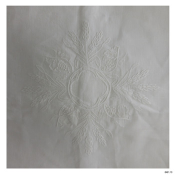 Embroidered white altar cloth has symbol of wheat wreath arranged around a circular central ring