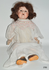 Doll has dark hair, porcelain face with brown eyes, open mouth with tooth, white dress, composite hands, brown shoes