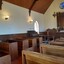 Two columns of wooden pews in rows of two pews arranged in the chapel with an aisle between