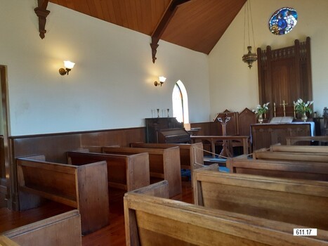 Two columns of wooden pews in rows of two pews arranged in the chapel with an aisle between