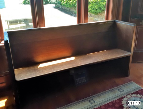 The pew is along the west wall facing inward to the club room and backrest next to window