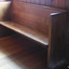 The pew is inside the doorway facing into the school room. It is along the east wall with the end against the north wall.
