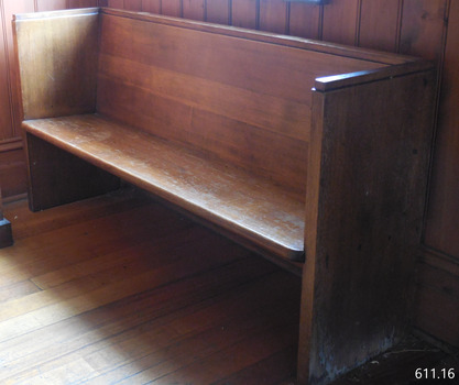 The pew is inside the doorway facing into the school room. It is along the east wall with the end against the north wall.