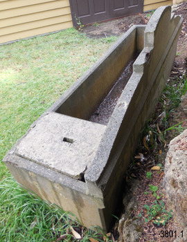 The base of the pediment is wider than its top and rests solidly on the trough’s base. There is some chipping on the top back of the pediment that shows the metal reinforcing inside it. 