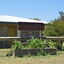 Horse trough is in front of the Warrnambool Pony Club sign. There is a grey brick building in the background. The trough is filled with green leafy plants.  The photograph was published in Wikimedia Commons, on a page called Bills Horse Troughs.