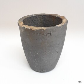 Grey crucible has sediment on the top edge and a stamp in the side