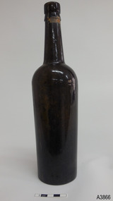 Tall slim dark coloured bottle with narrow neck. Glass is shiny. Remnants of tape and wire around the neck.