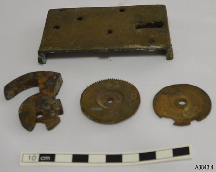 Loch frame and cogs, plus a lever, are on a table. Holes in the fram show where parts were attached.