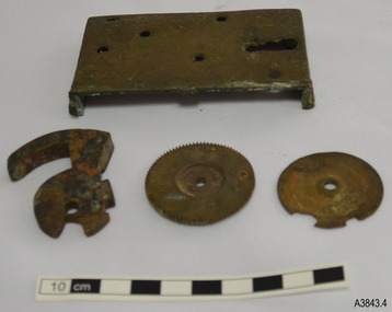 Loch frame and cogs, plus a lever, are on a table. Holes in the fram show where parts were attached.