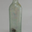 Tall, clear glass bottle. Shoulder seam. Cork has fallen into base. Glass shows opalescence. Encrustation on surface.