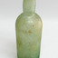 Tall clear glass Bottle with green tinge. Some encrustation on surface. Bulbous neck. Body tapers inwards towards base. 