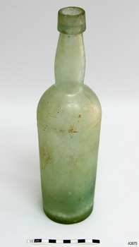 Tall clear glass Bottle with green tinge. Some encrustation on surface. Bulbous neck. Body tapers inwards towards base. 