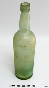 Tall clear glass Bottle with green tinge. Some encrustation on surface. Bulbous neck. Body tapers inwards towards base. 
