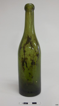Shiny green glass bottle standing upright. Bottle has blob top. Sediment is inside the bottle.
