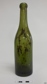 Shiny green glass bottle standing upright. Bottle has blob top. Sediment is inside the bottle.