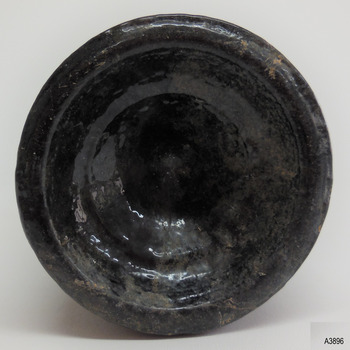 Base has an uneven heal. Surface of glass is bumpy and glass is discoloured. Base is pushed in and there is a pontil mark.