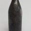 Black glass bottle has flared collar and chip on its lip. Sides are not symmetrical. Glass has imperfections.