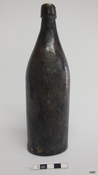 Black glass bottle has flared collar and chip on its lip. Sides are not symmetrical. Glass has imperfections.