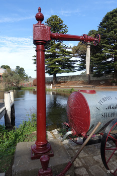 Crimson painted water standpipe with decorative finial on top. Outlet hose is above Furphy cart.