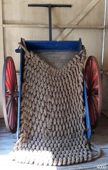 Wooden cart painted blue and white, with red metal wheels and a woven rope cover
