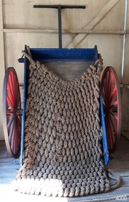 Wooden cart painted blue and white, with red metal wheels and a woven rope cover