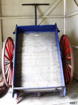 Cart is resting on its backboard, handle in the air. Base and sides are made of planks of wood. 