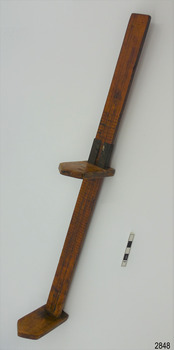 Wooden hem marker stand, leaning, with marking arm about half of the way up.