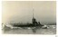 Black and white photograph of a battleship, bow stirring up the water