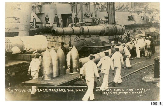 Sailors in white, beside ammunition,  sailors in dark uniform on ship beside them
