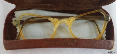 Brown hard case with opaque yellow spectacle frames and blue cleaning cloth