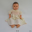 Doll has moulded head and limbs, open mouth with two teeth, and is wearing a cream dress with pink smocking