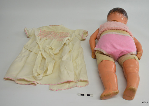 Doll has a fabric body and is dressed in underwear. The doll's dress is on the bench.