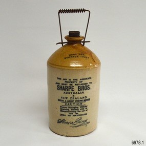 Earthenware bottle has inscriptions, coiled wire handle and flat-topped stopper