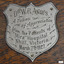 Silver metal plaque in a shield shape is engraved with test and fancy border
