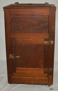 Wooden ice chest with lid on top, door at front and flap between front feet