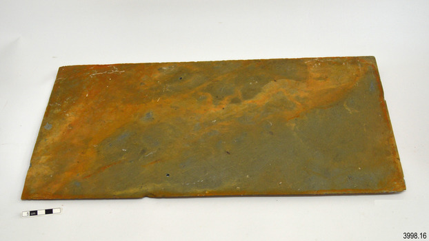 Tile has two holes drilled through. It has strong orange-brown stain over grey colour.