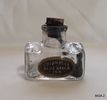 Glass ink bottle has label, cork, and remnants of dried ink