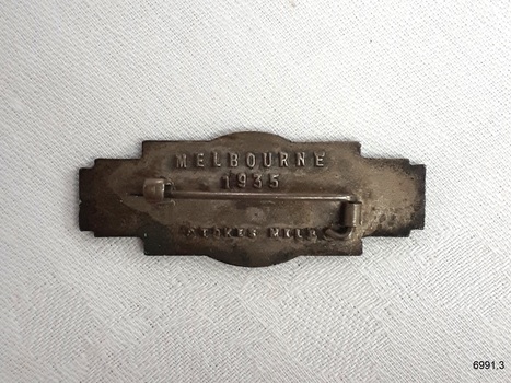 Badge has a long pin for attaching it, and embossed lettering.