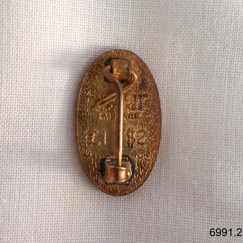 Back has embossed inscription and vertical pin.
