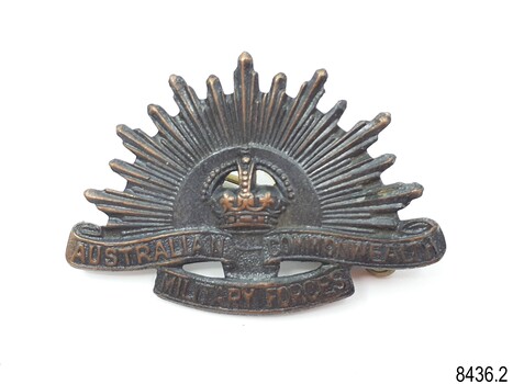 Badge has crown, sunrays and inscription on ribbon design