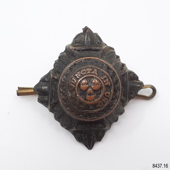 Metal badge is diamond-shaped. It has an inscription and three crown logos.