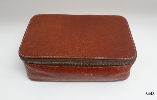 Pouch is tan leather with a brass zipper around three sides